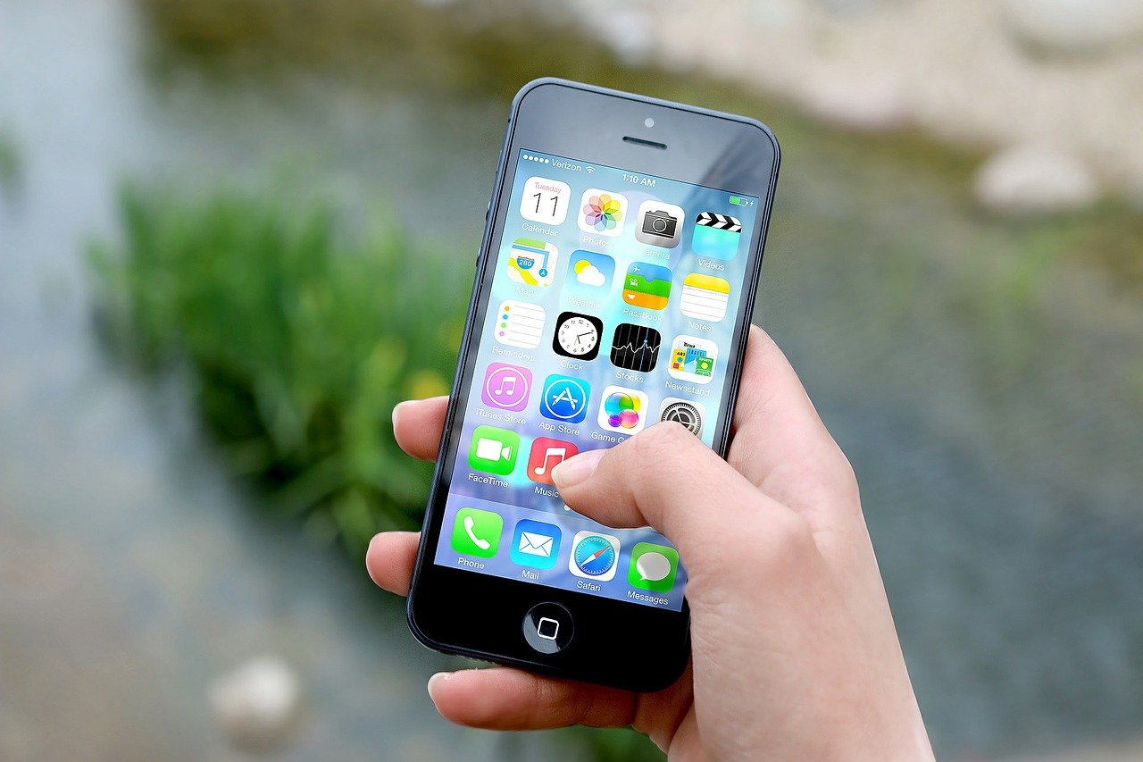A hand holds an iPhone outdoors, showcasing the best iPhone for kids with various app icons brightly displayed on the screen.
